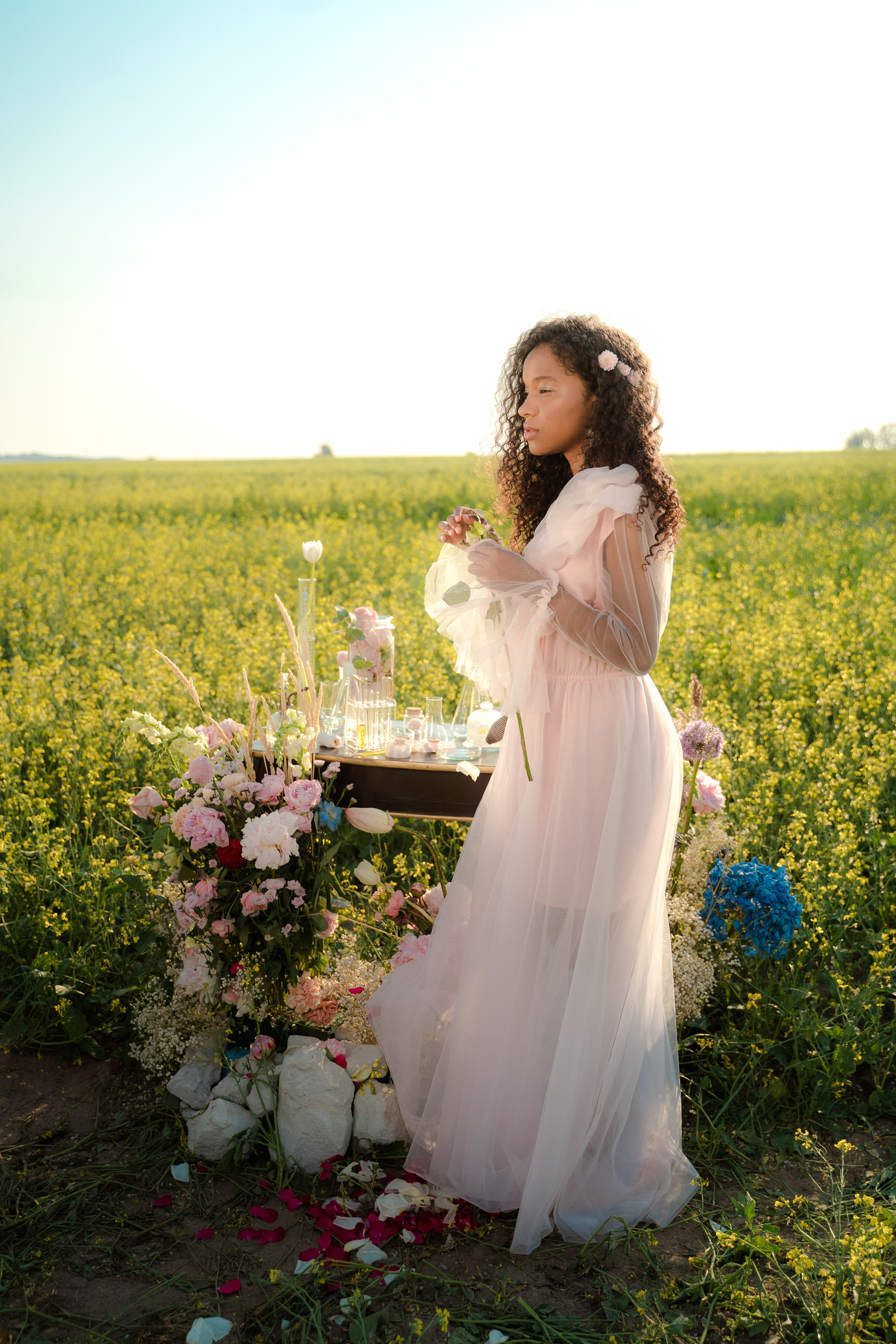 Woman in Tulle Dress Standing in Flower Field Next to Glass Laboratory Equipment
